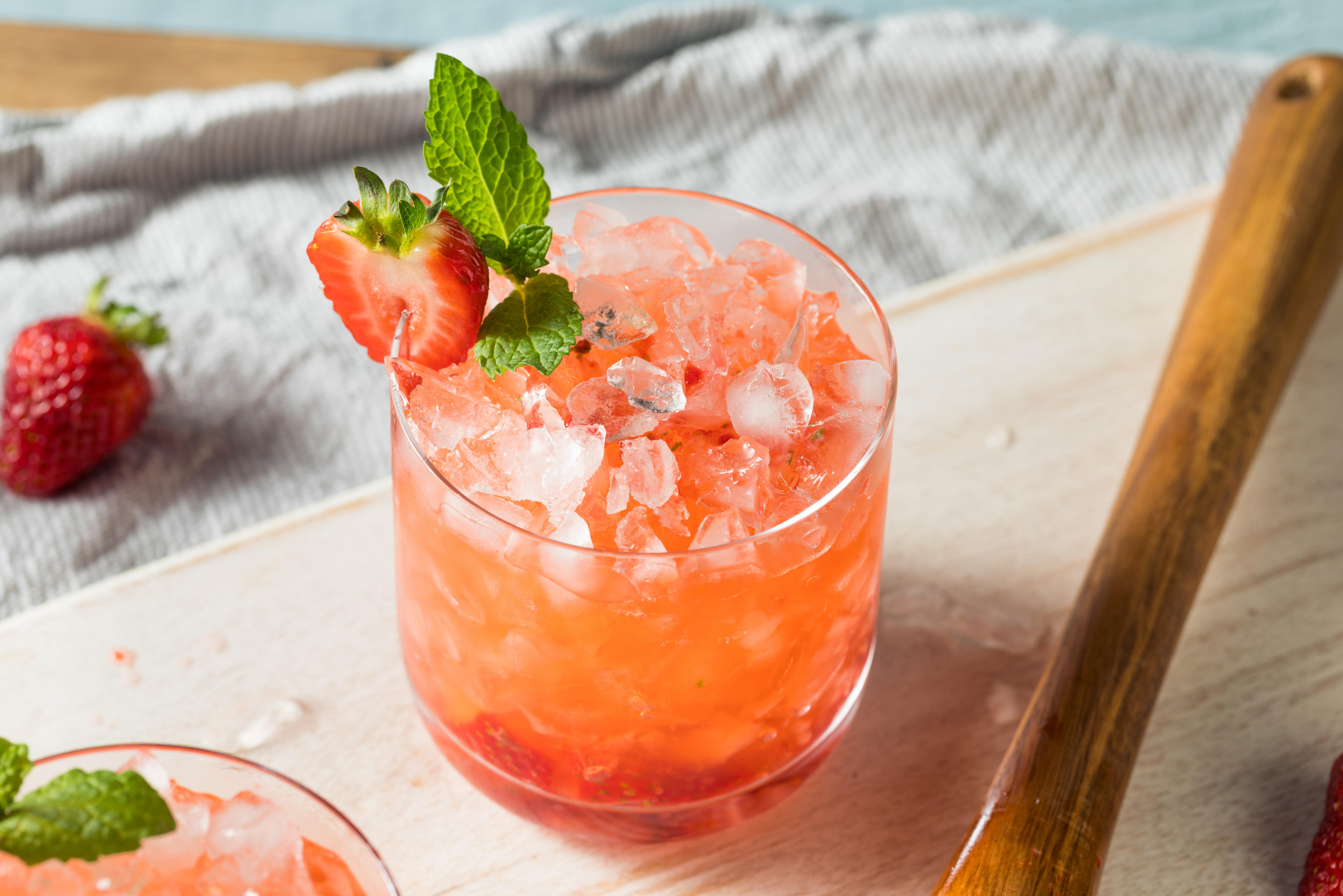 glass of Strawberry Basil Smash on a tray beside a wooden ladle and a strawberry