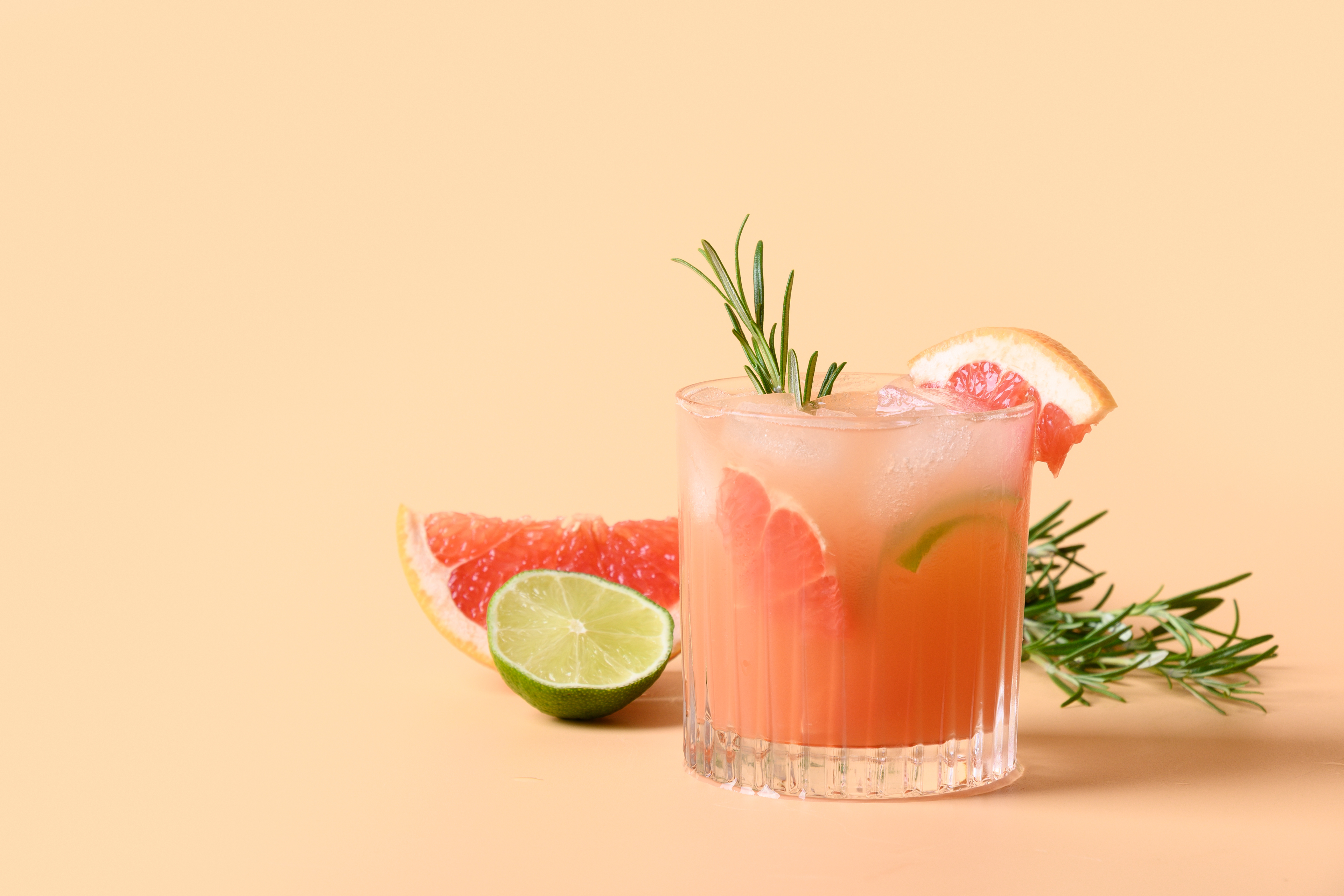 glass of Grapefruit Paloma surrounded by rosemary sprigs, grapefruit and lime slices