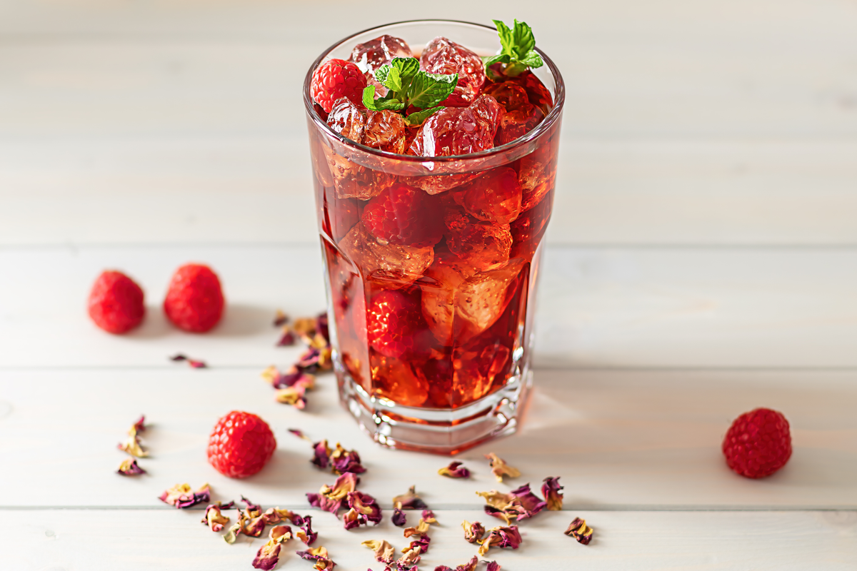 a glass of Raspberry Hibiscus Tea surrounded by dried hibiscus flowers and 4 raspberries