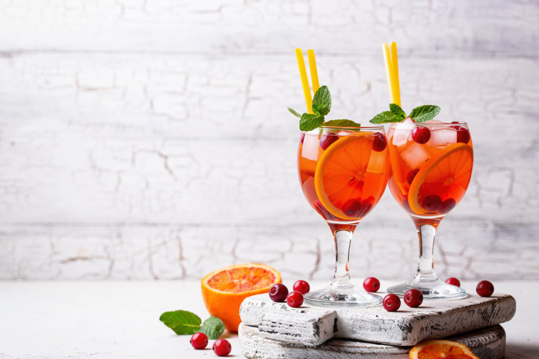 2 glasses of Cranberry Orange Spritz on a white chopping board among cranberries and orange slices