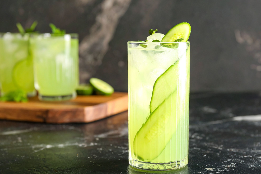 glass of Cucumber Mint Cooler with a tray of Cucumber Mint Coolers in the background
