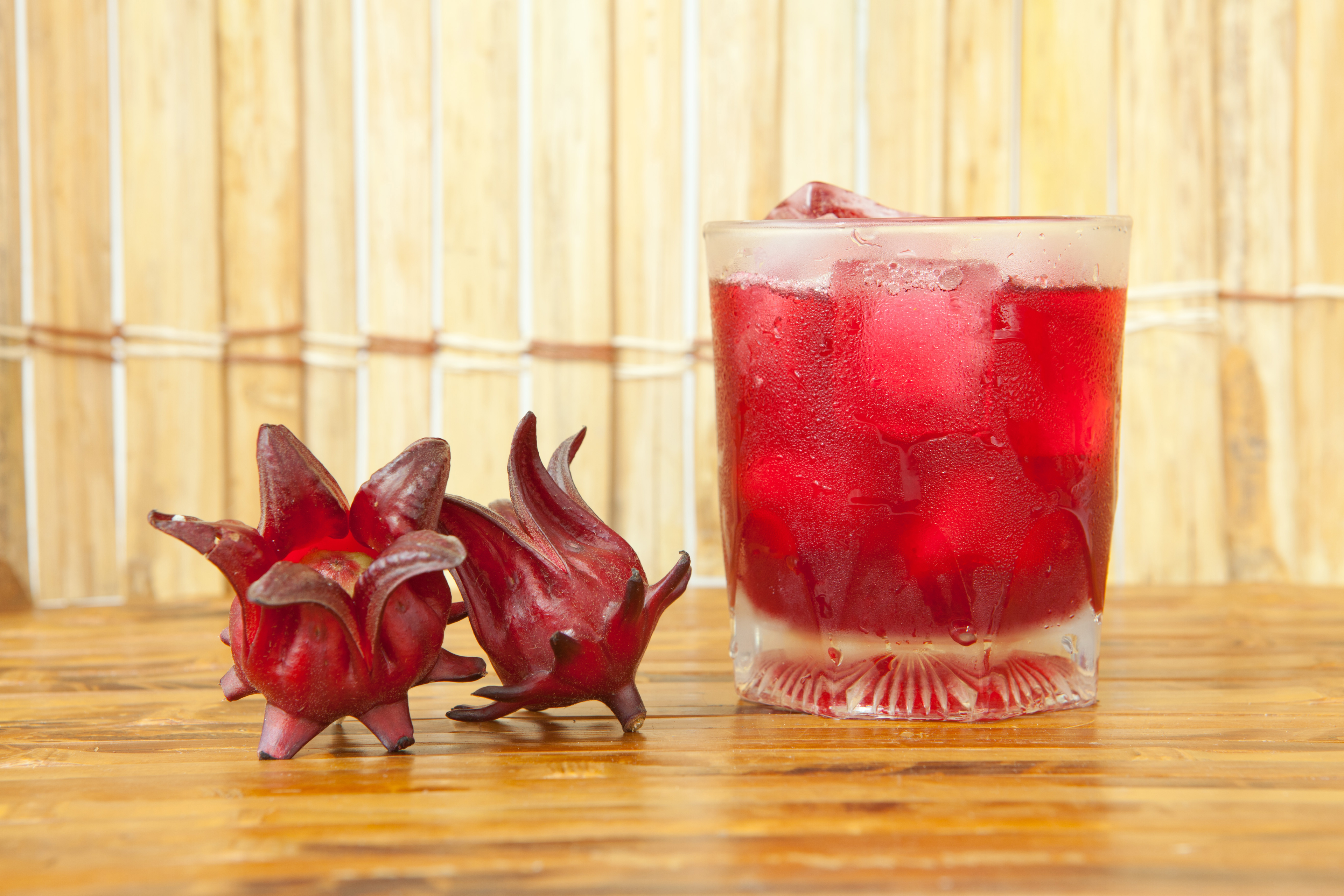 glass of Iced Hibiscus Tea beside two red Hibiscus sabdariffa buds
