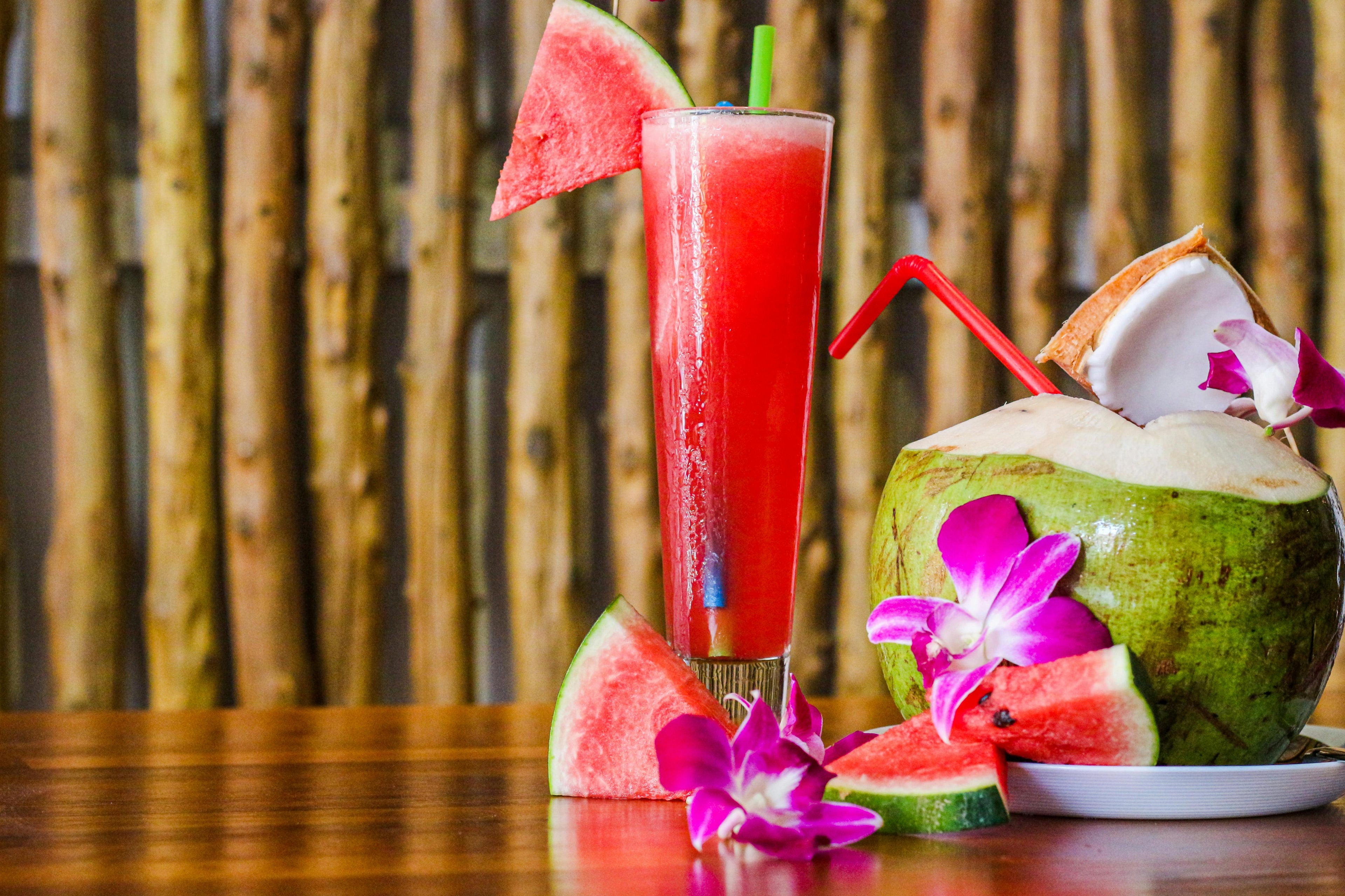 tall glass of Watermelon Agua Fresca garnished with watermelon slices beside a coconut with a straw