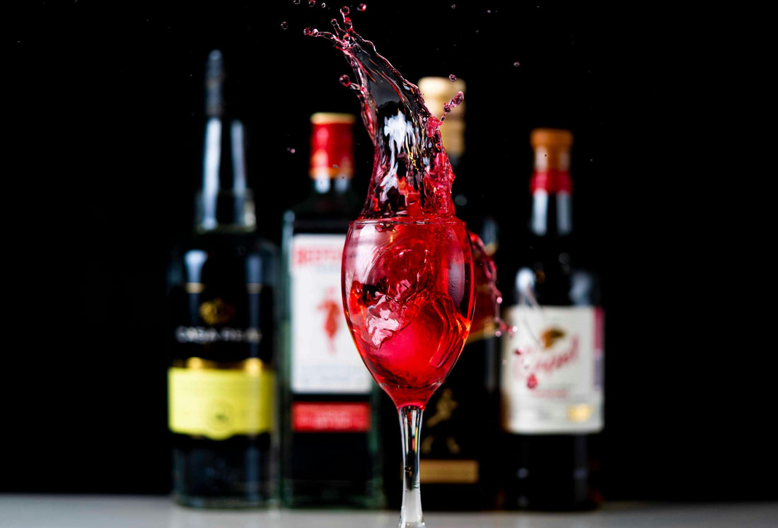 a wine glass with wine splashing out of it set against a backdrop of liquor bottles
