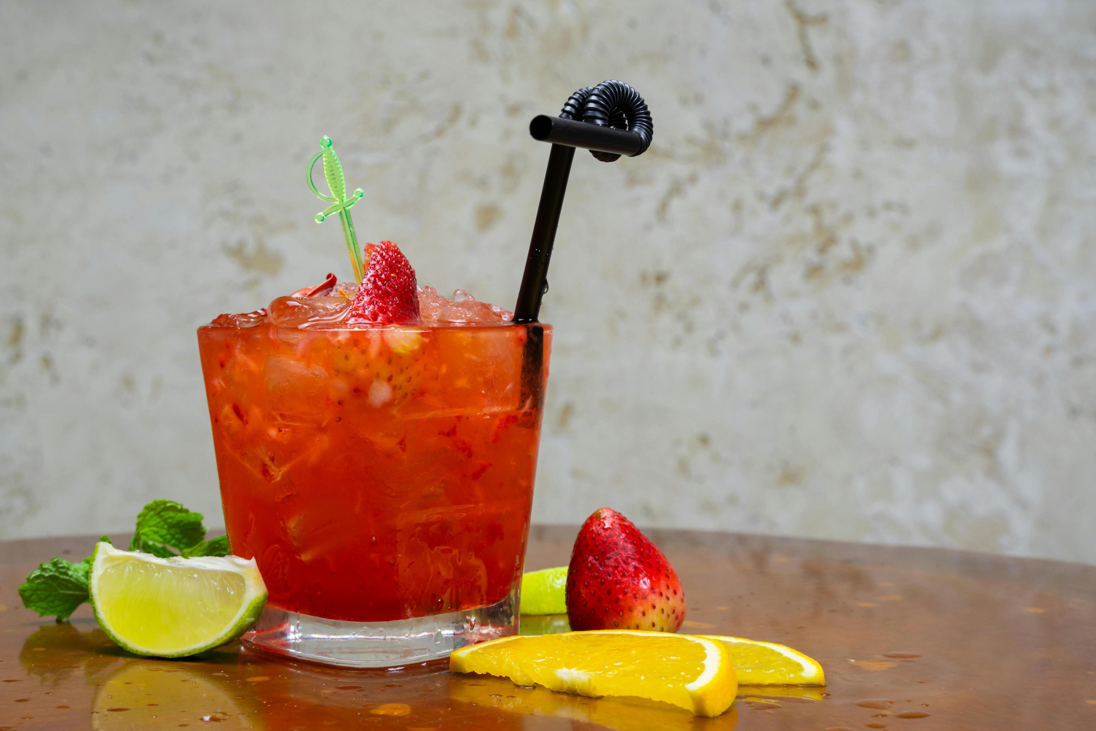 glass of Strawberry Lemonade Spritzer with a black straw surrounded by a strawberry, lime, and lemon