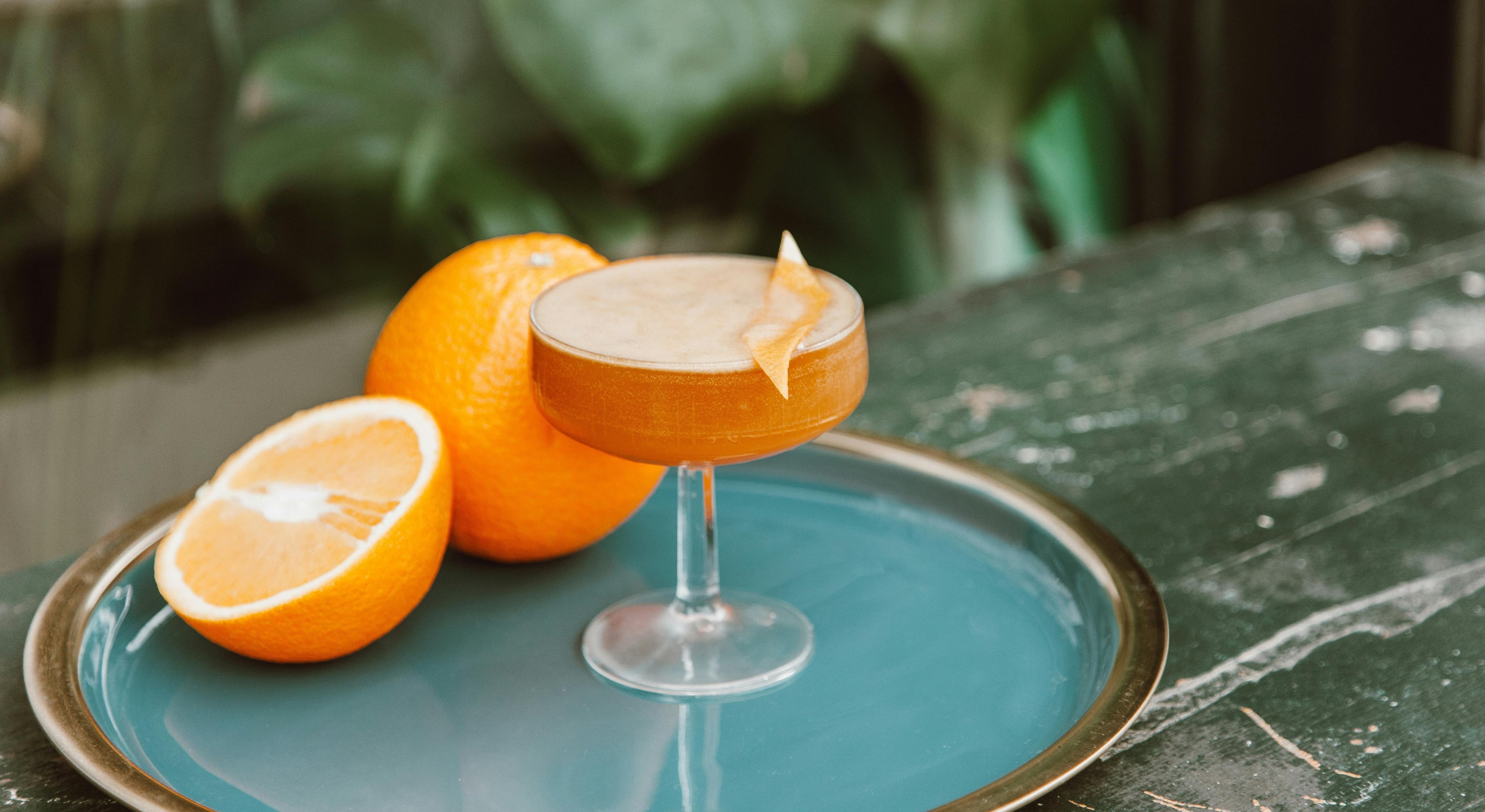wine glass of Orange Creamsicle Mocktail on a blue tray with oranges