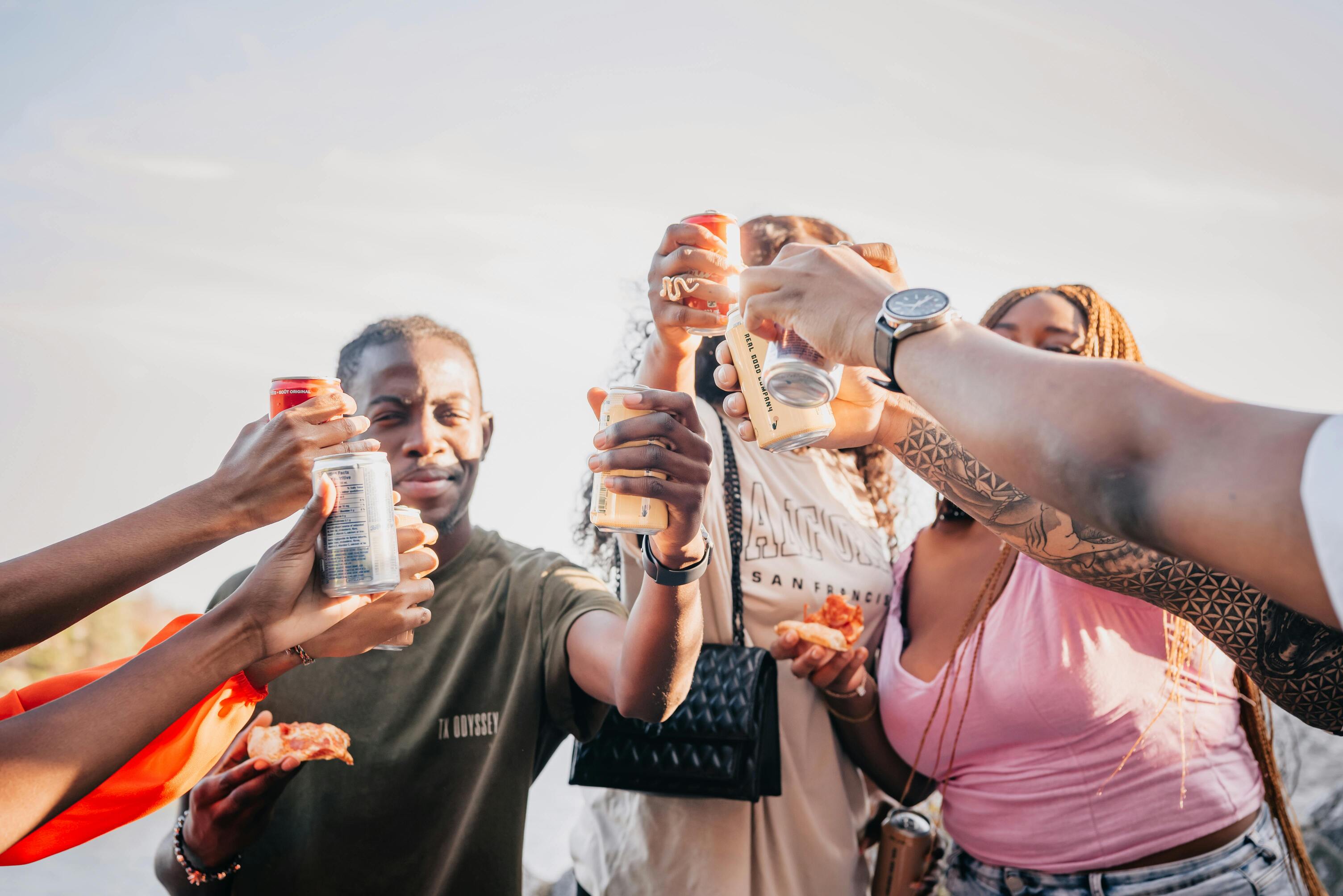 a group of friends clinking their canned THC drinks together at a music festival